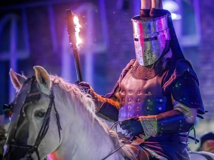 A masked knight on horseback holding a torch